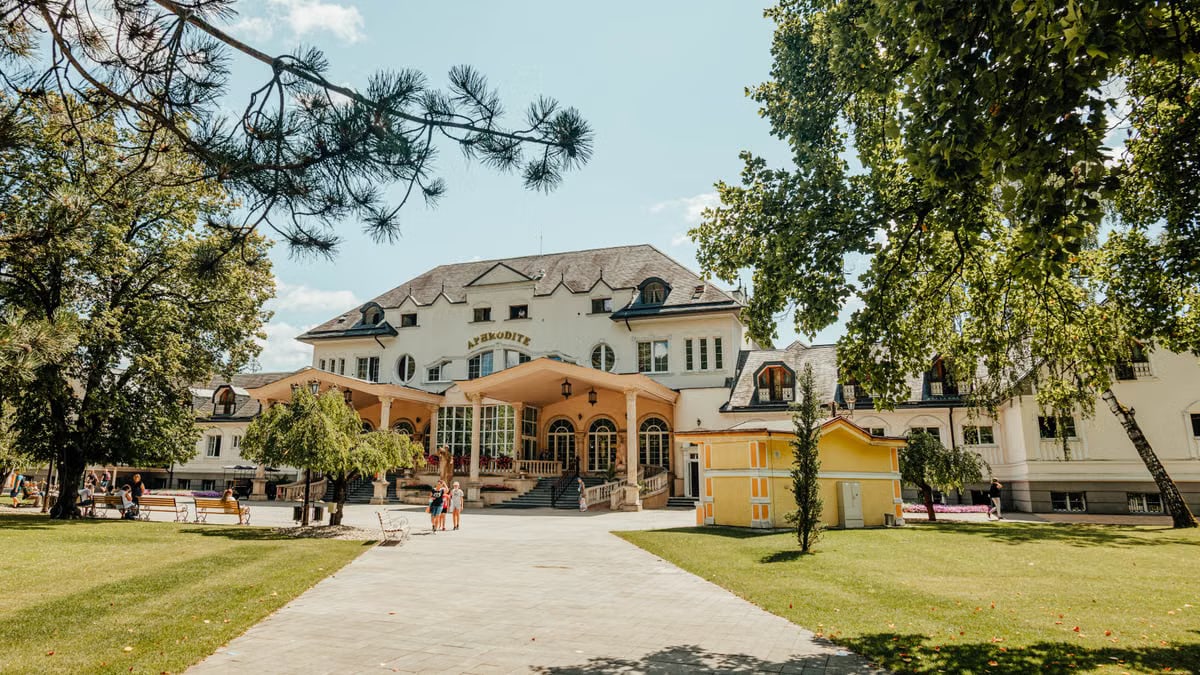 Elegant historic building amidst lush gardens under a bright blue sky.